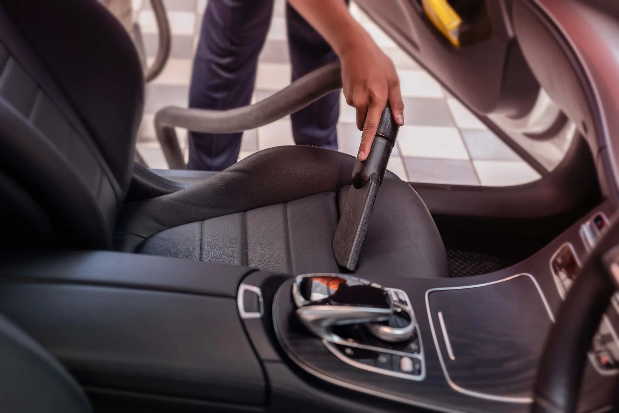 Technician vacuuming car interior during professional detailing service